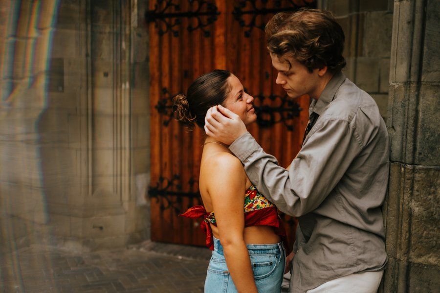 Couple facing each other in historic alley with ornate red doors, warm golden light