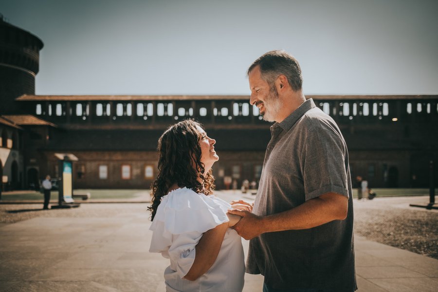 Couple smiling together in sunlit courtyard at Sforzesco Castle in Milan