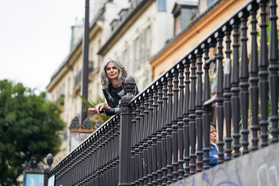 Woman with gray hair leaning on ornate black railing on Parisian building balcony, daytime