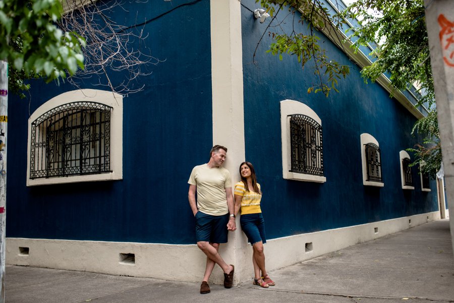 couple holding hands in front of bright blue colonial building with ornate windows in coyoacán