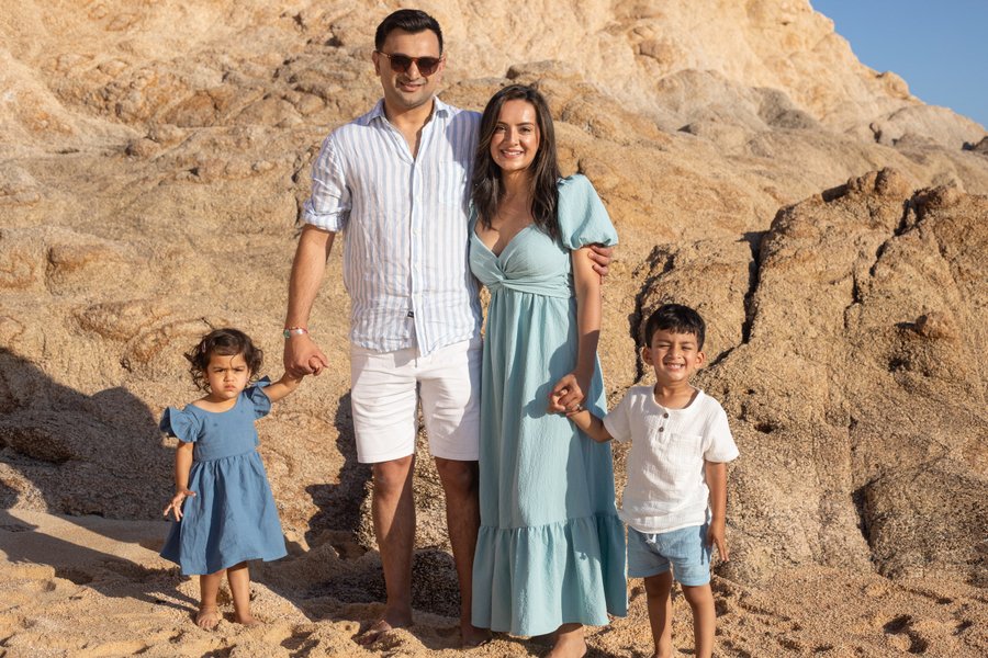 Family of four smiling in front of massive golden rock formation at El Arco, Cabo San Lucas in bright daylight