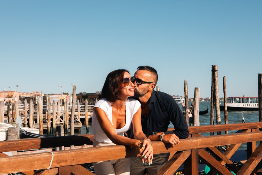 Couple kissing on wooden dock overlooking Venice's historic mooring poles and lagoon in bright daylight
