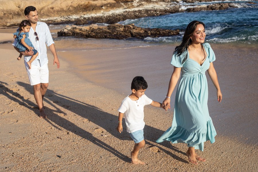 Family walking on sandy beach at sunset with rocky coastline and blue waves in background