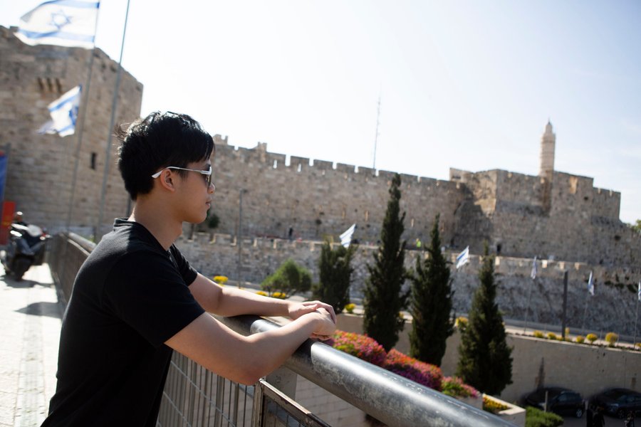 Solo traveler overlooking Jerusalem's ancient stone walls and David's Tower at Jaffa Gate in bright daylight