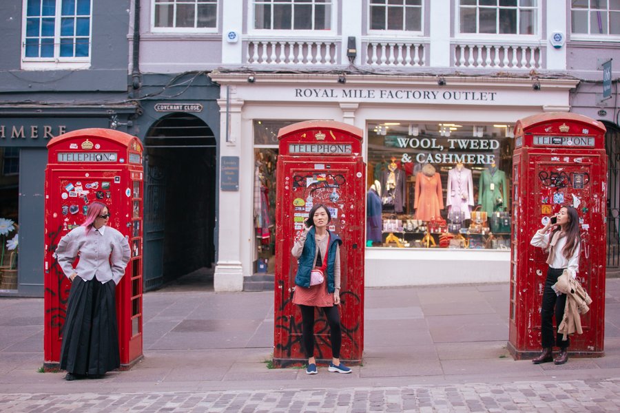 Three women pose with iconic red British telephone boxes outside a wool and cashmere shop in Edinburgh's old town
