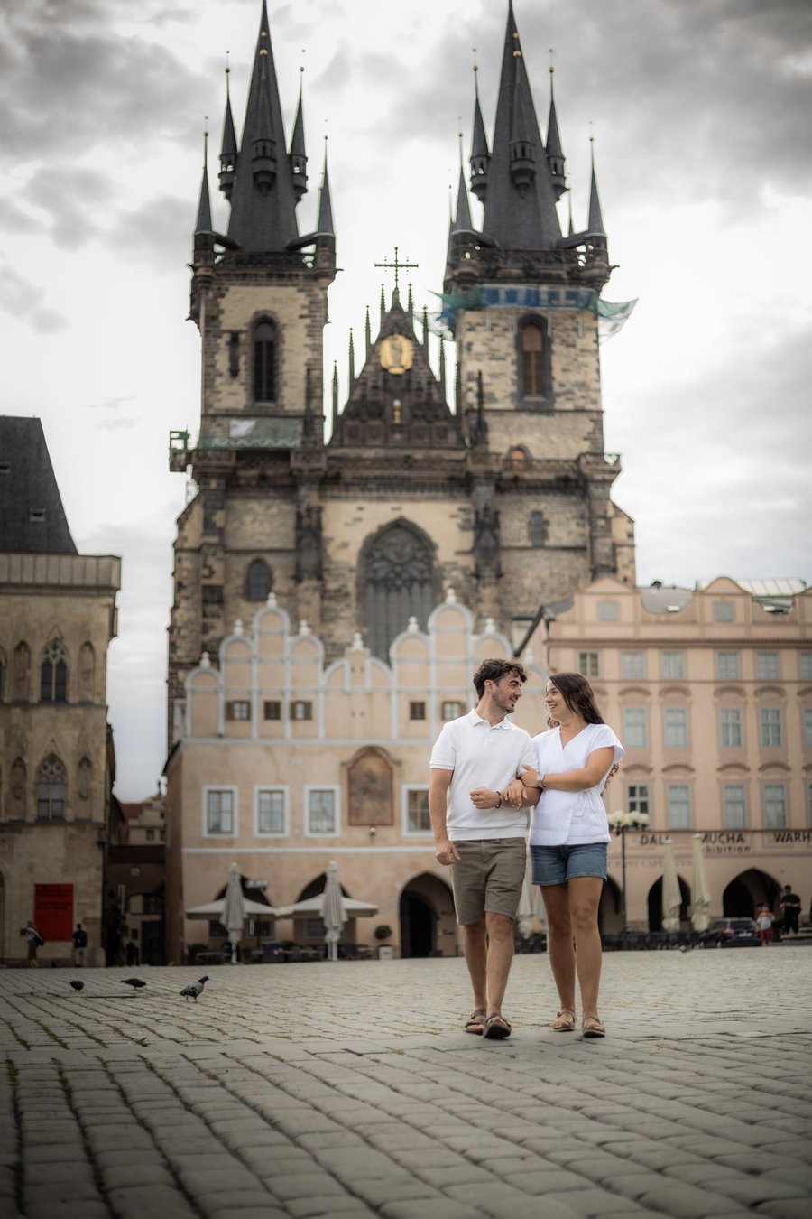 Couple in white shirts standing arm-in-arm in Prague's Old Town Square with the Church of Our Lady before Tyn in the background