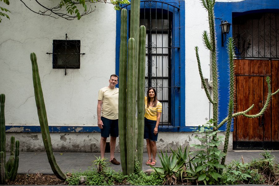 Couple posing among tall cacti in front of a blue and white colonial building in Coyoacán, Mexico City