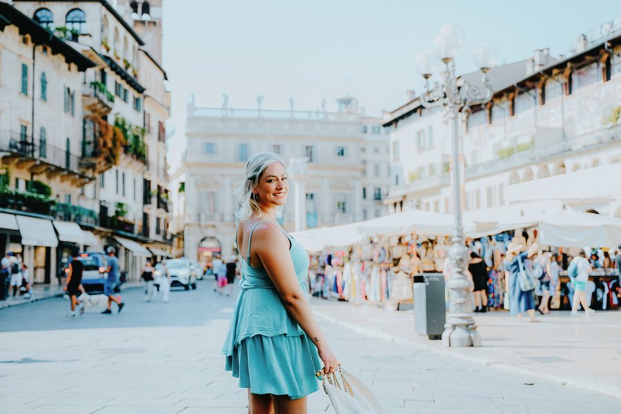 Woman in turquoise dress poses in sunlit Italian piazza surrounded by Renaissance architecture