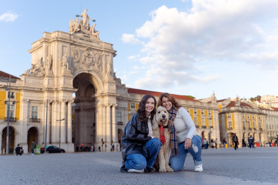 Two women with a terrier dog posing at Praça do Comércio in Lisbon, historic arch and yellow buildings behind them