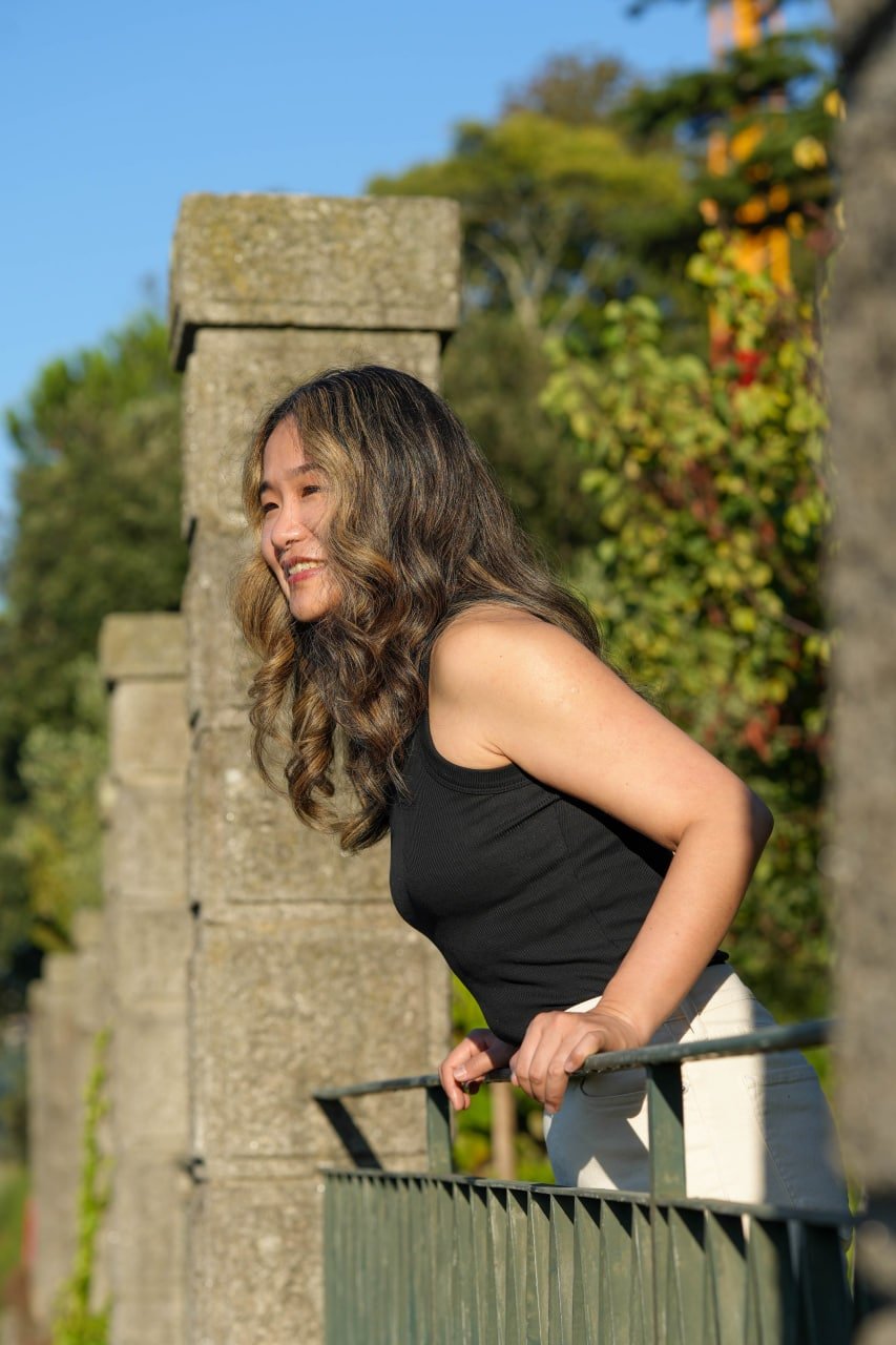 Solo woman posing at ivy-covered stone ruins in sunlit garden with clear blue sky