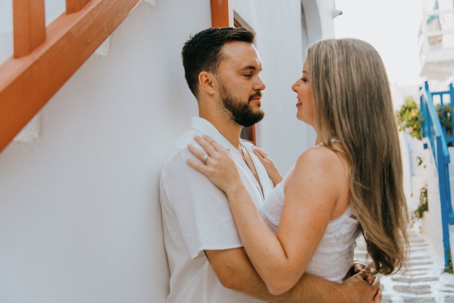 Couple in white outfits embracing against whitewashed walls in Mykonos Town during daytime
