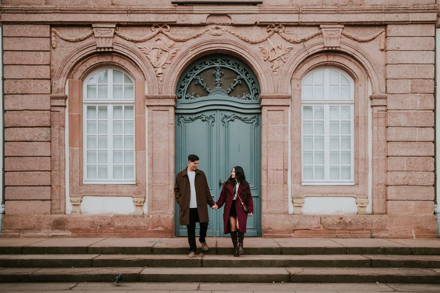 couple holding hands in front of ornate historic building with green door and arched windows in colmar