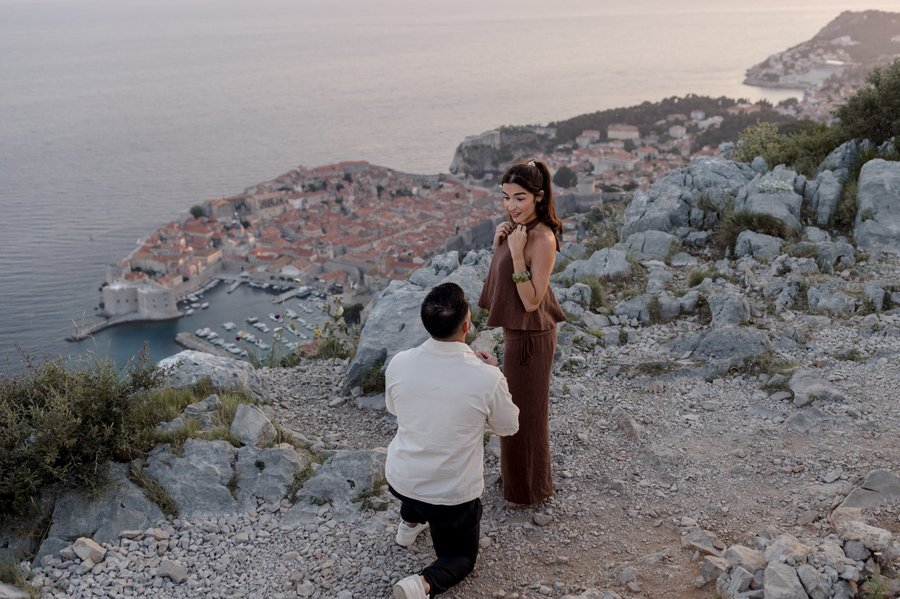 Couple on rocky clifftop overlooking Dubrovnik's terracotta rooftops and Adriatic Sea at golden hour