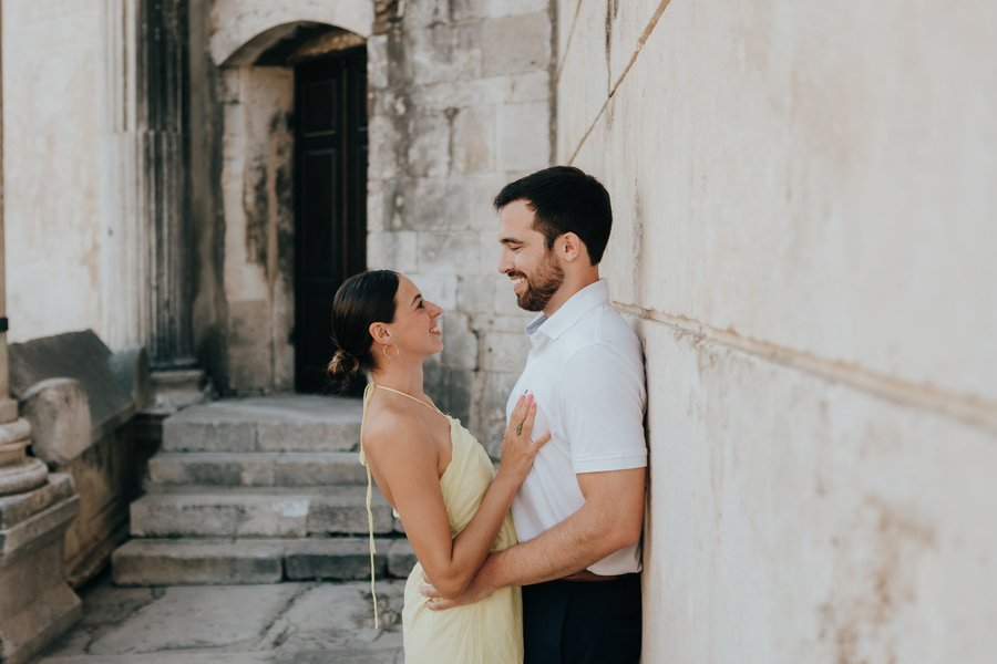 couple embracing in a narrow historic alleyway with weathered stone walls and arched doorways
