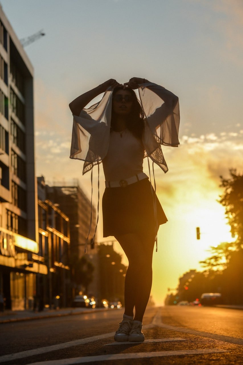 Solo woman with sheer fabric posed on urban street at golden hour sunset