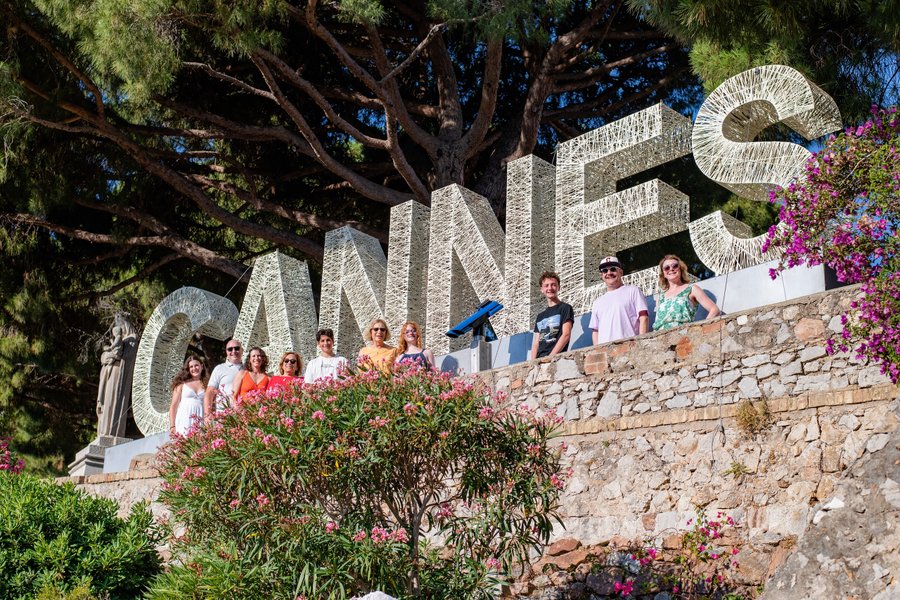 Group of tourists posing at large stone letters on La Croisette promenade in Cannes under bright sunlight