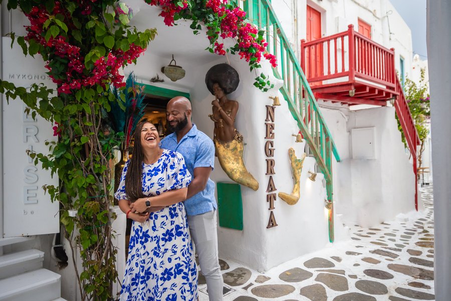couple posing among vibrant bougainvillea flowers in mykonos town's charming whitewashed alley