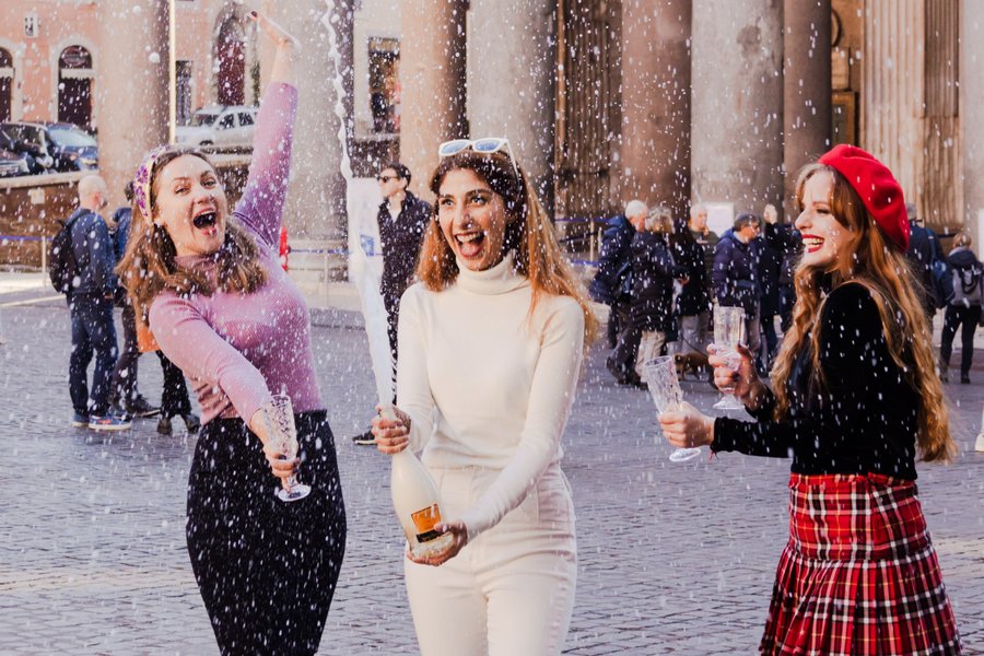Three women celebrating with champagne in falling snow outside the Pantheon in Rome