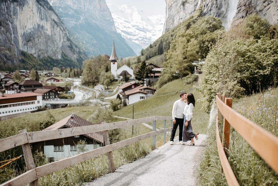Couple walking on a mountain path in Interlaken valley with snow-capped peaks and church spire visible below