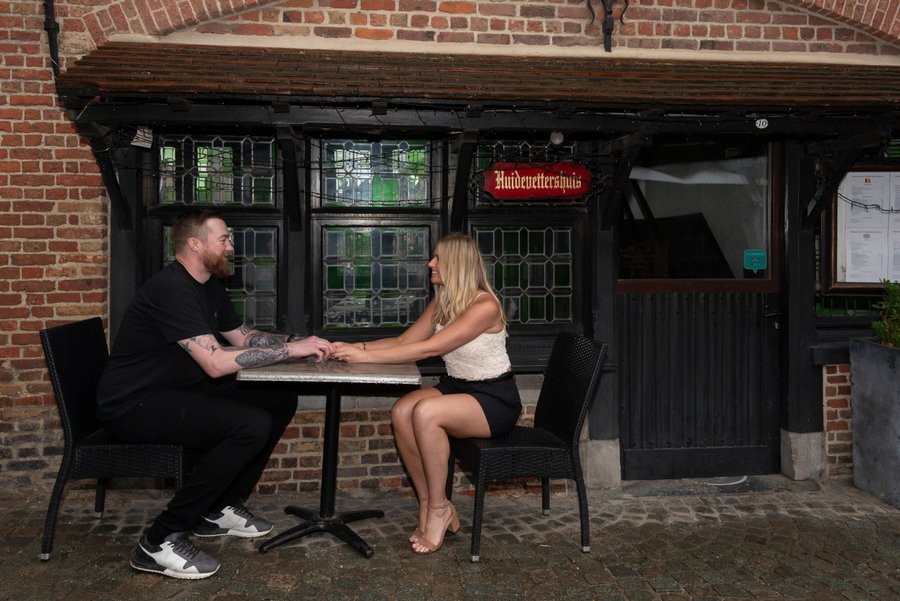 Couple holding hands at a small table outside a traditional brick building in Bruges during daytime