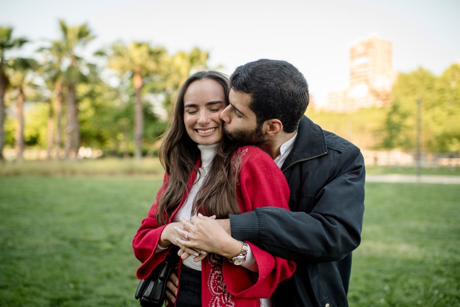 Couple embracing in a park with palm trees and city buildings under warm afternoon light