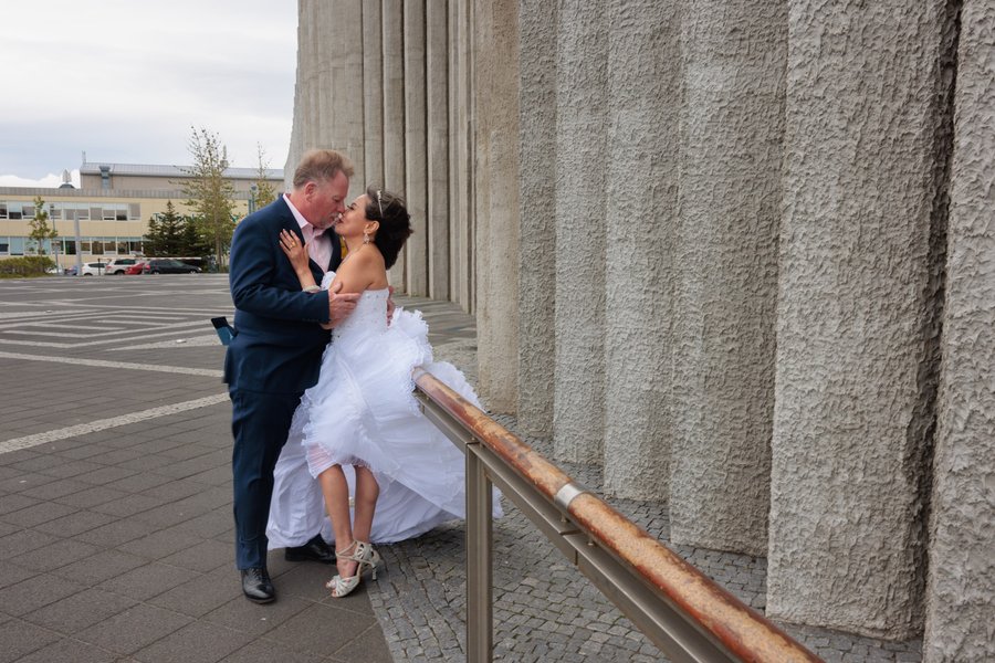 Couple kissing by concrete columns at Hallgrímskirkja, bride in white dress and groom in navy suit