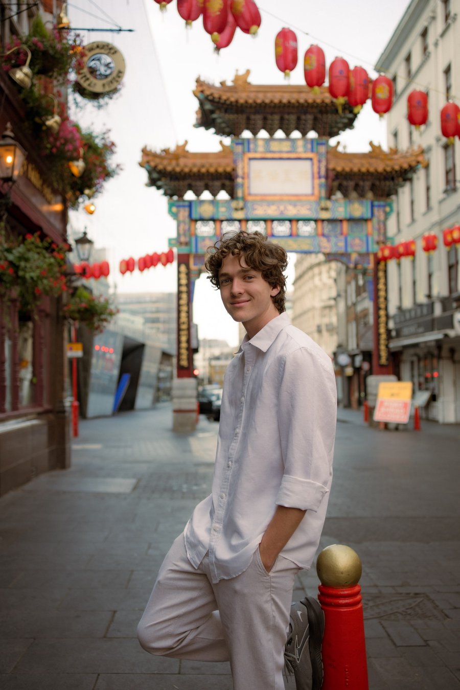 Solo traveler in white shirt poses in London's Chinatown with ornamental gate and red lanterns overhead