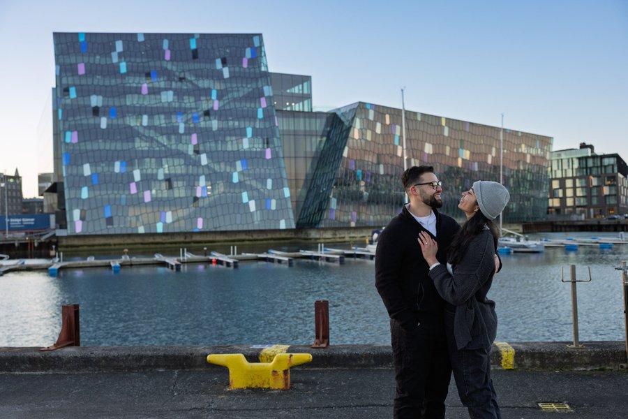 Couple in winter coats gazing at modern harborside architecture with colorful glass facade in Reykjavík