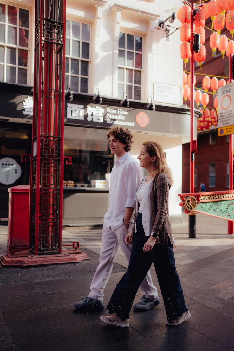 Couple walking through London's Chinatown street decorated with red lanterns and traditional architecture during daytime