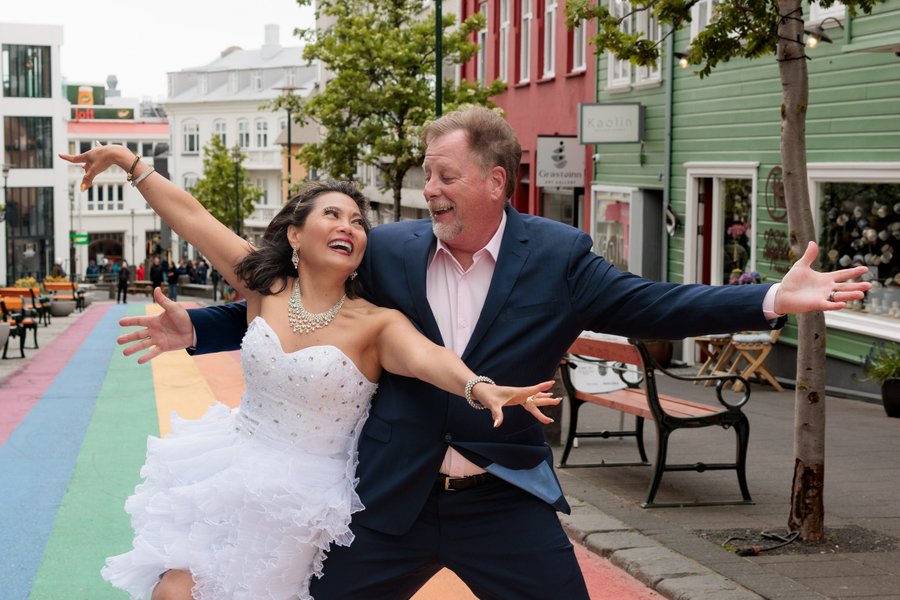 Couple celebrating on a colorful street in downtown Reykjavík with historic buildings and green trees in daylight