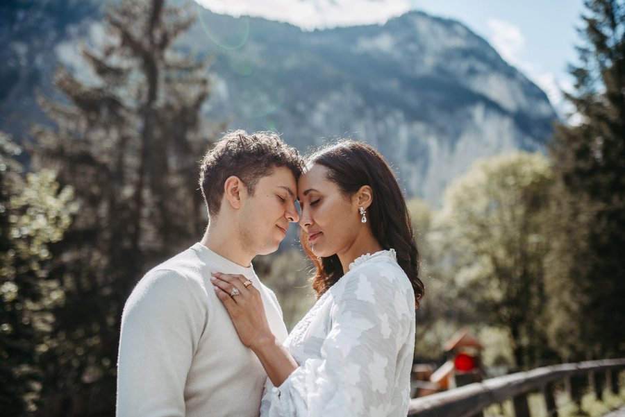 Couple embracing with foreheads touching in alpine valley, mountains and evergreen forest behind them