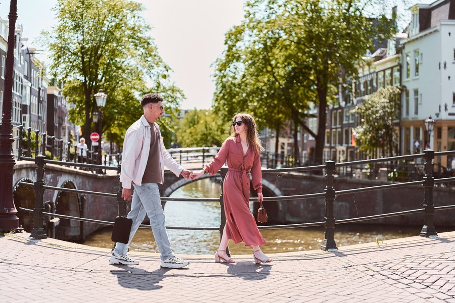 Couple holding hands on a bridge over an Amsterdam canal lined with trees on a sunny day
