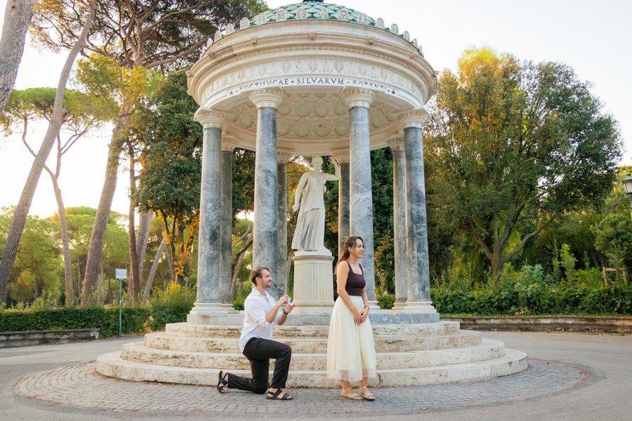 man proposing to woman at classical columned gazebo in rome's villa borghese gardens during golden hour
