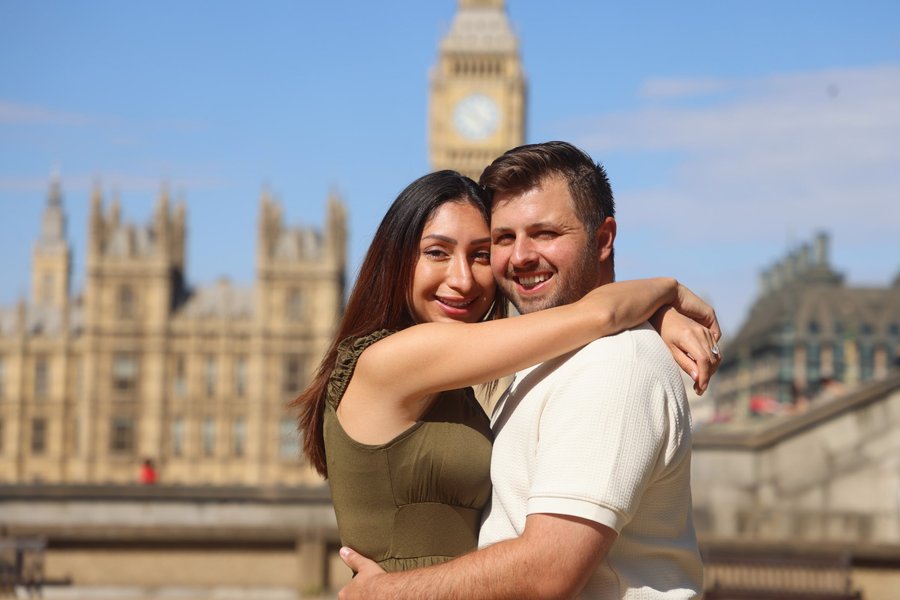 Couple embracing by the Thames with Big Ben and Palace of Westminster in background, London daytime