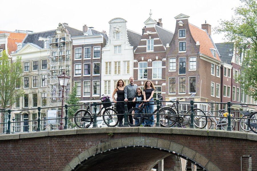 Group of four on a canal bridge with bicycles, historic Dutch townhouses and waterway behind them during daytime